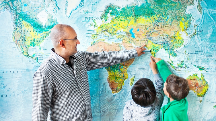 En manlig lärare med glasögon och rutig skjorta visa världskarta för två lågstadieelever. Foto: Scandinav Bildbyrå/Astrakan