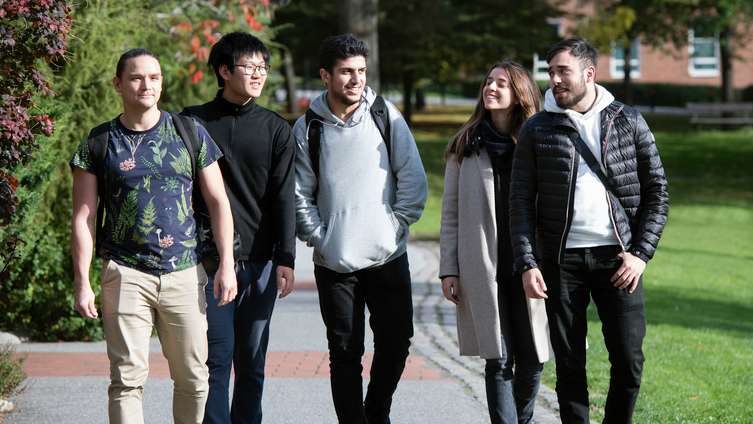 Fem studenter går i en park på väg till universitetet