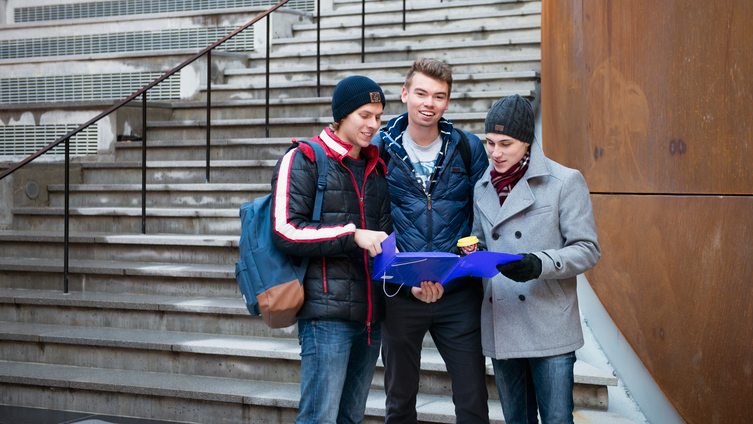 Tre studenter i vinterkläder står framför trappan till ett universitet