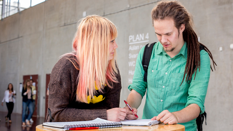 Två studenter går igenom sina anteckningar vid ett bord i entrén på en högskola